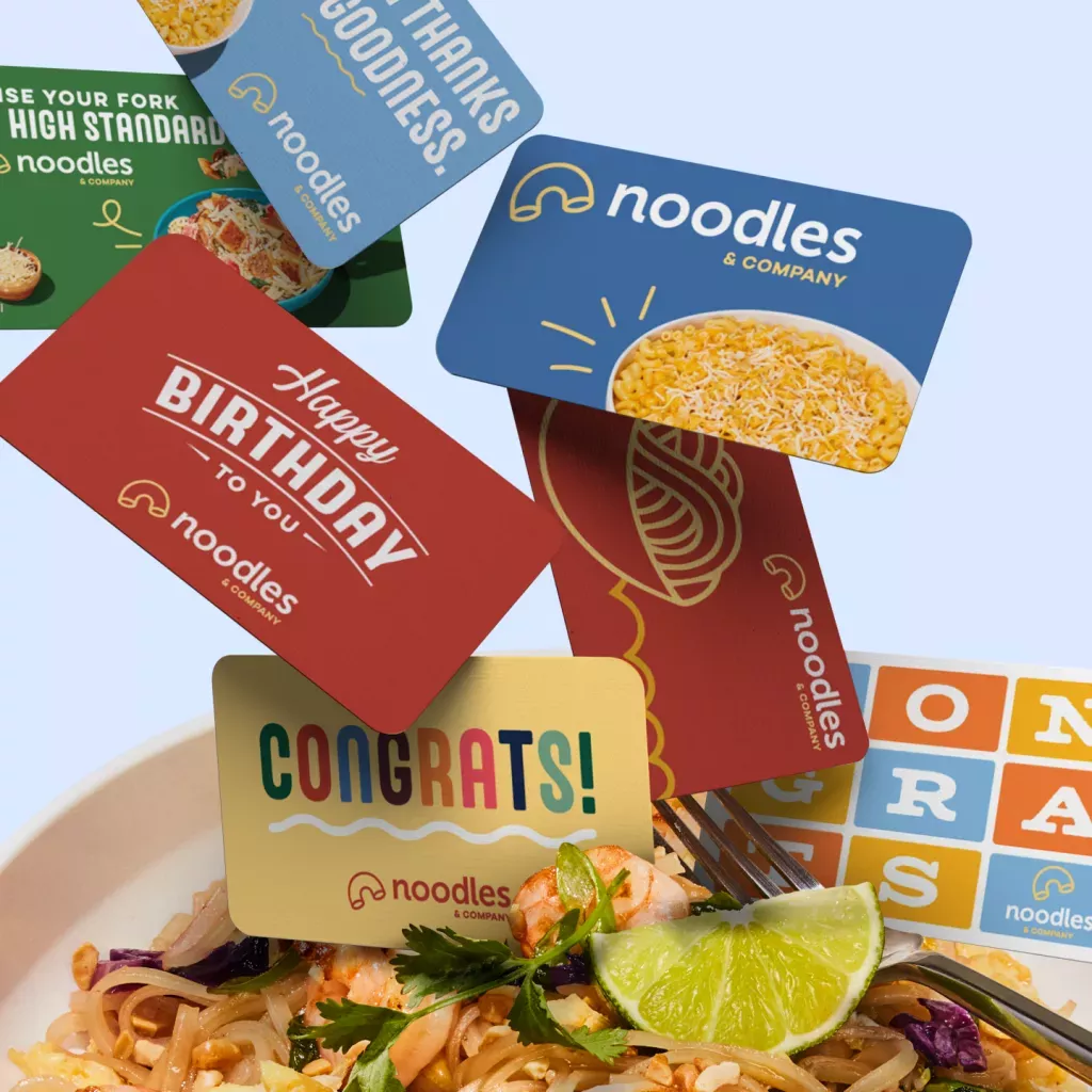 Noodles & Company gift cards falling into a bowl of Pad Thai.