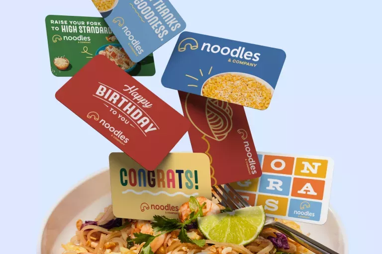 Noodles & Company gift cards falling into a bowl of Pad Thai.