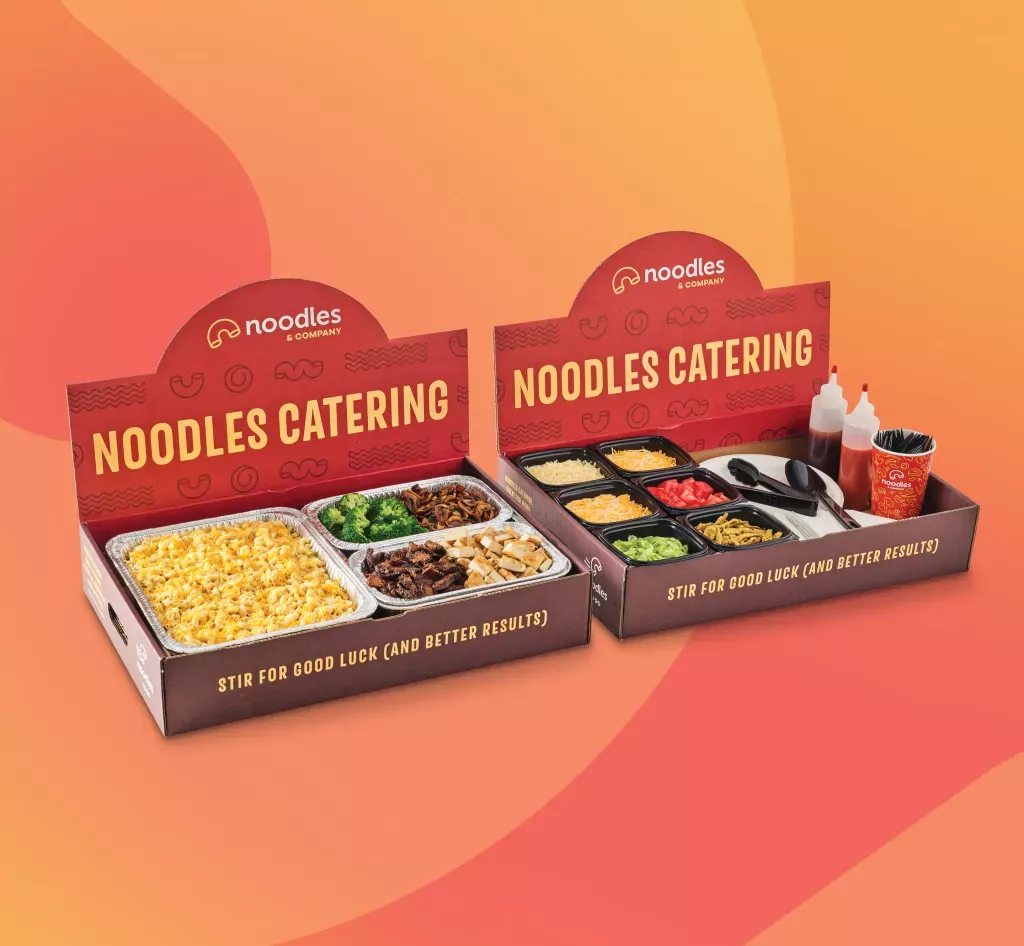 Noodles and Company Mac Bar catering box that includes pan of macaroni and cheese, two protein options and various toppings options.