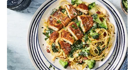 Crispy Chicken Bacon Alfredo. Dish show on a decorative plate with a glass of water in a blue glass.