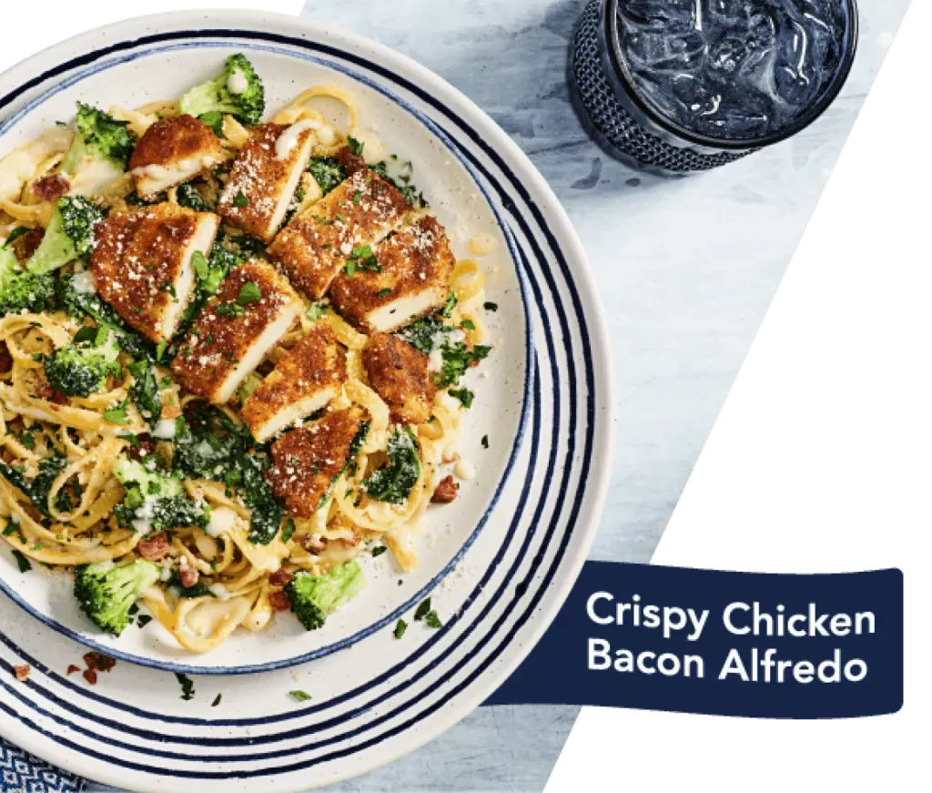 Crispy Chicken Bacon Alfredo. Dish show on a decorative plate with a glass of water in a blue glass.