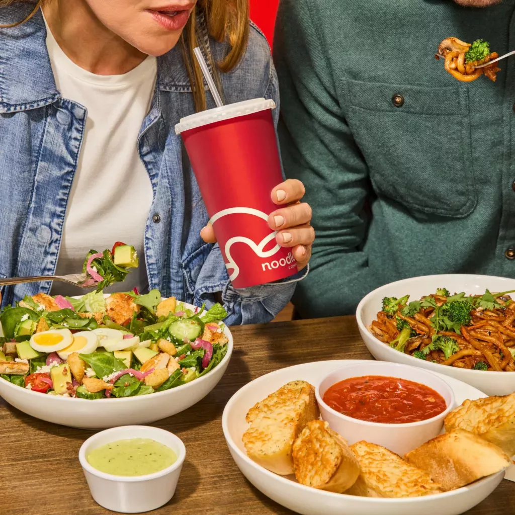 Woman and man enjoying a Green Goddess Cobb Salad, Japanese Pan Noodles and Cheesy Garlic Bread