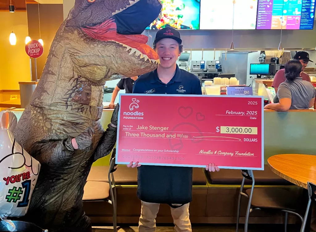 Noodles and Company 2025 Scholarship Award Winner holding a large check.