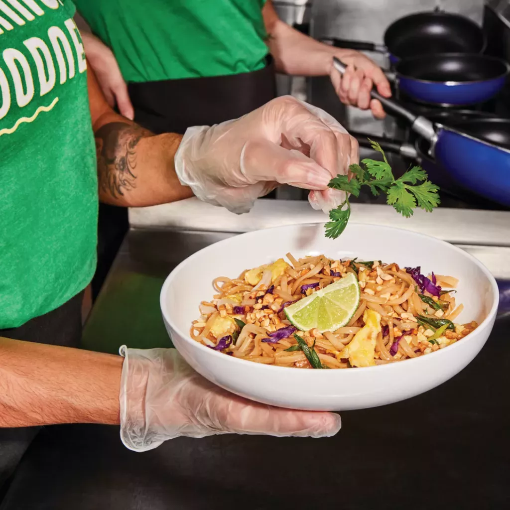 Noodles & Company Team Member garnishing a bowl of Pad Thai with Cilantro