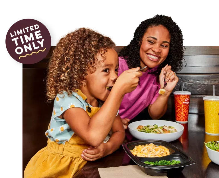 Limited Time Only. Kid eating a Noodles Kids Wisconsin Mac and Cheese with Broccoli next to her Mom enjoying a Zucchini Pesto with Grilled Chicken dish and a fountain drink.