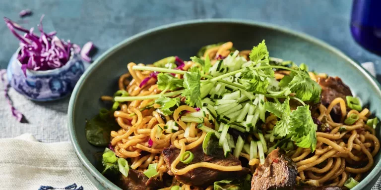 Spicy Korean Steak Noodles in a green bowl, with fresh sliced cucumber and cilantro on top