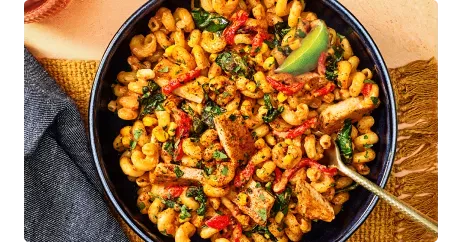 Chipotle Chicken Cavatappi in dark blue bowl with a fork and napkin.