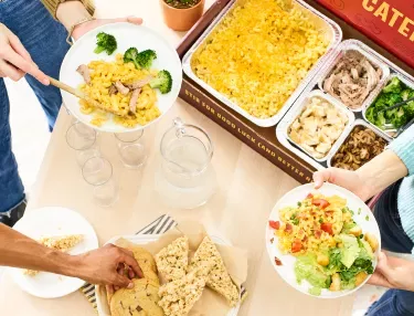 catering table top with an assortment of dishes and desserts and people filling their plates