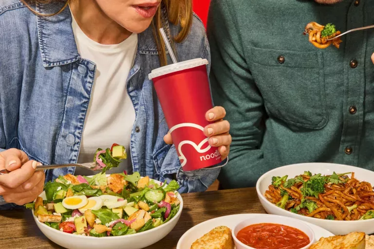 Woman and man enjoying a Green Goddess Cobb Salad, Japanese Pan Noodles and Cheesy Garlic Bread