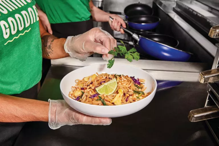 Noodles & Company Team Member garnishing a bowl of Pad Thai with Cilantro